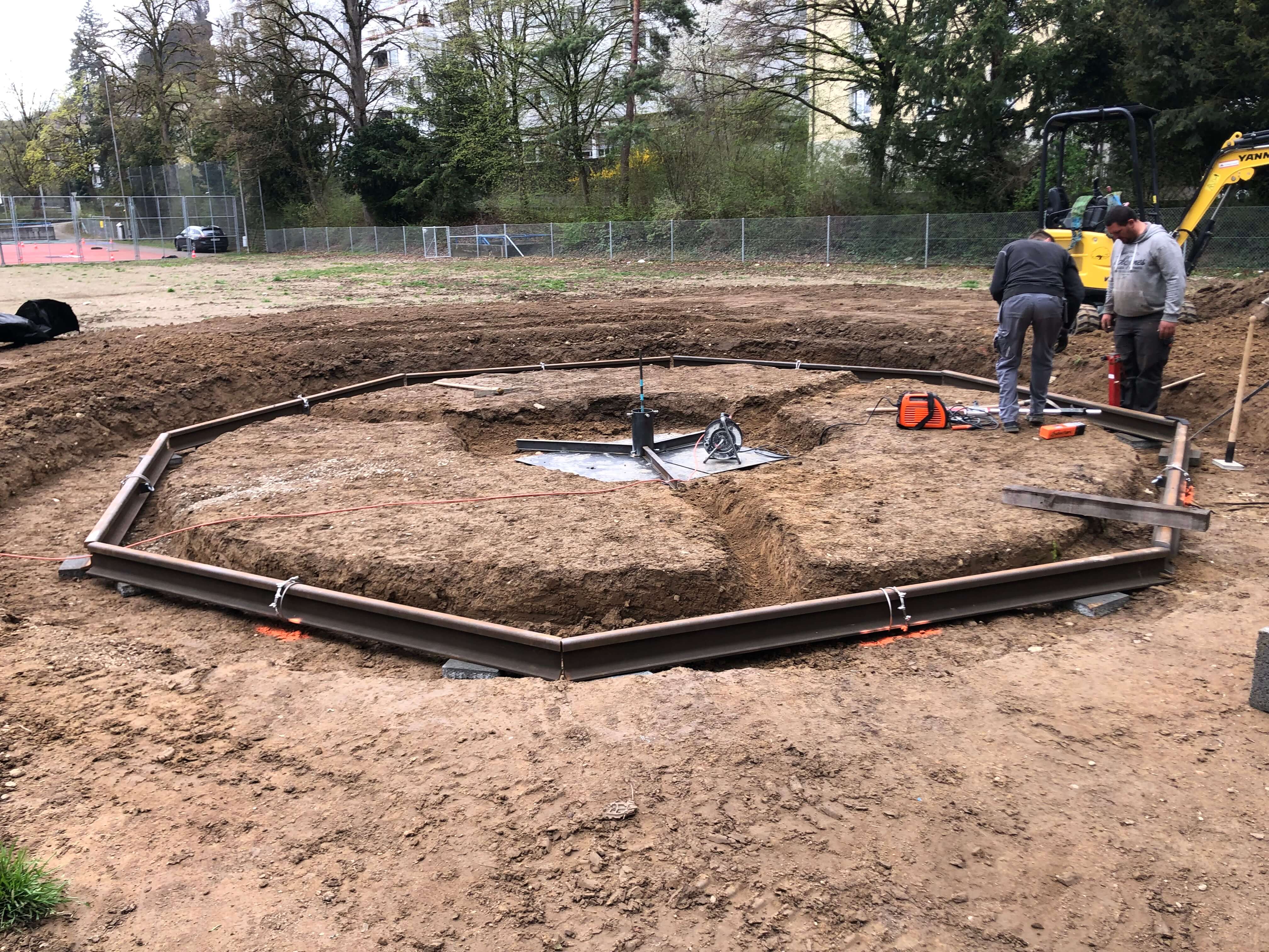 Deux ouvriers travaillent à la construction d'une base circulaire en gravier sur un chantier en plein air.