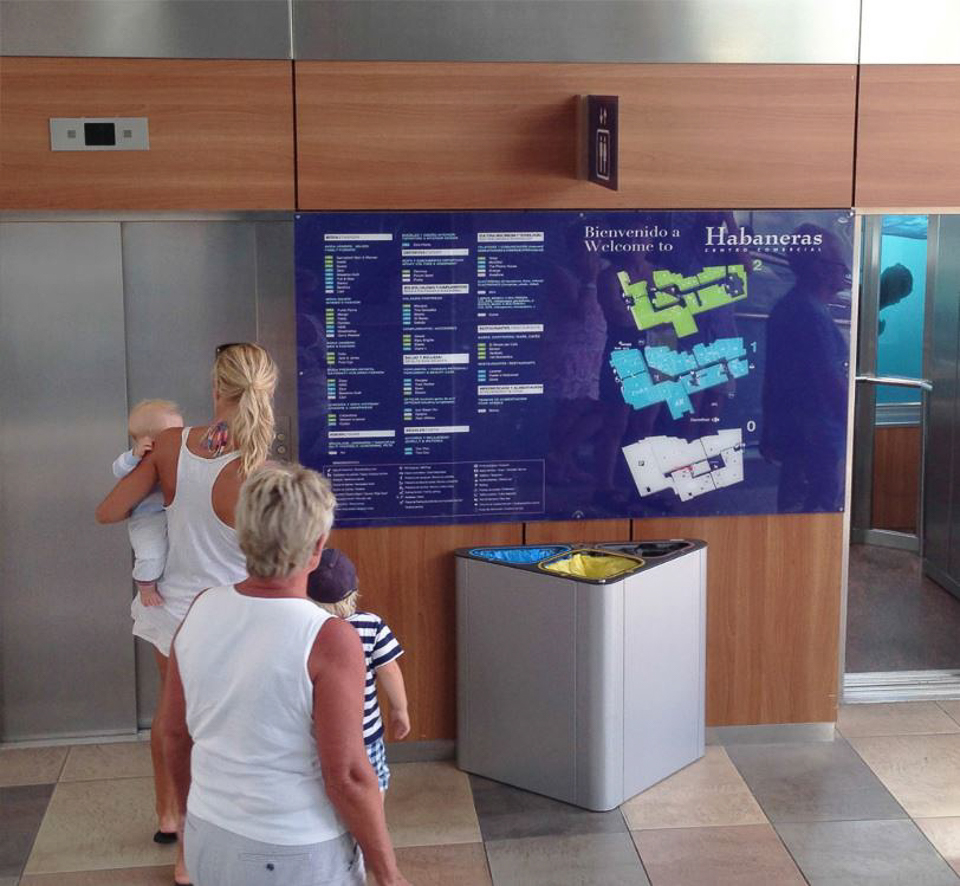 Eine Familie steht vor einem Übersichtsplan im Einkaufszentrum Habaneras neben einem Aufzug und einem Mülleimer