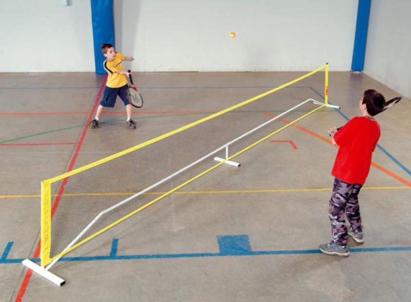 Zwei Kinder spielen Tennis in einer Sporthalle mit einem tragbaren Netz