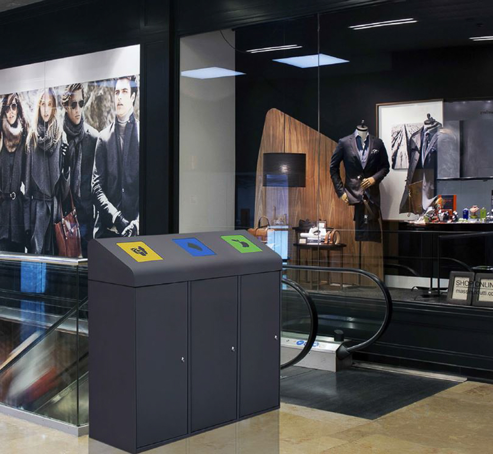 Drei nebeneinander stehende Mülleimer zur Abfalltrennung vor einem Schaufenster mit stilvoll gekleideten Mannequins in einem Einkaufszentrum.
