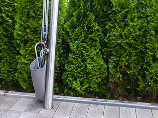 Douche d'extérieur en acier inoxydable placée devant des haies vertes sur une terrasse en bois