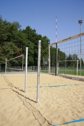 Ein Beachvolleyballfeld mit Netz und Sand umgeben von Bäumen und blauem Himmel