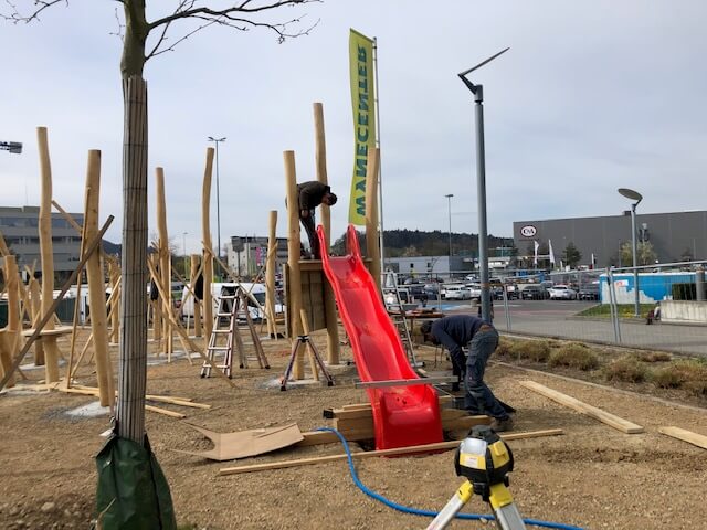 Construction d'une aire de jeux avec structures en bois et toboggan rouge, ouvriers lors du montage