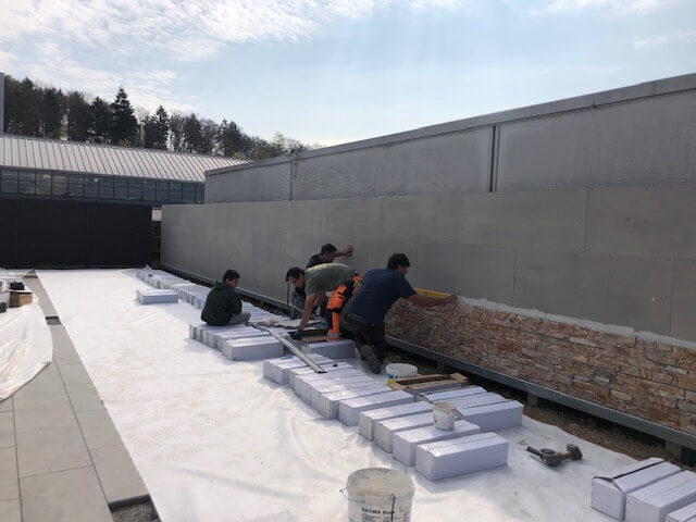 Plusieurs ouvriers posent du carrelage sur un mur à l'extérieur sur un grand chantier.