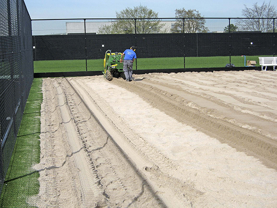 Un ouvrier utilise une machine pour répartir le sable sur un court de tennis.