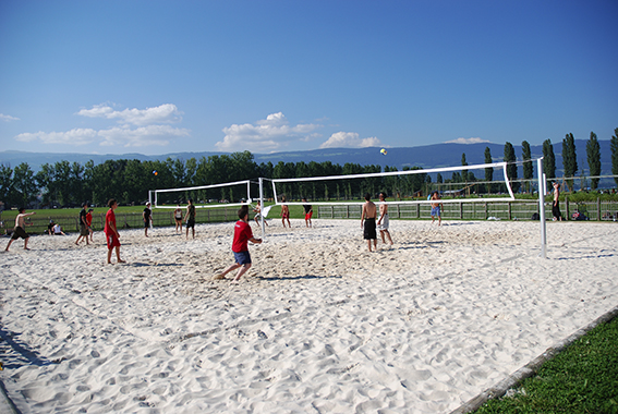 Menschen spielen Beachvolleyball auf einem Sandplatz unter klarem blauem Himmel