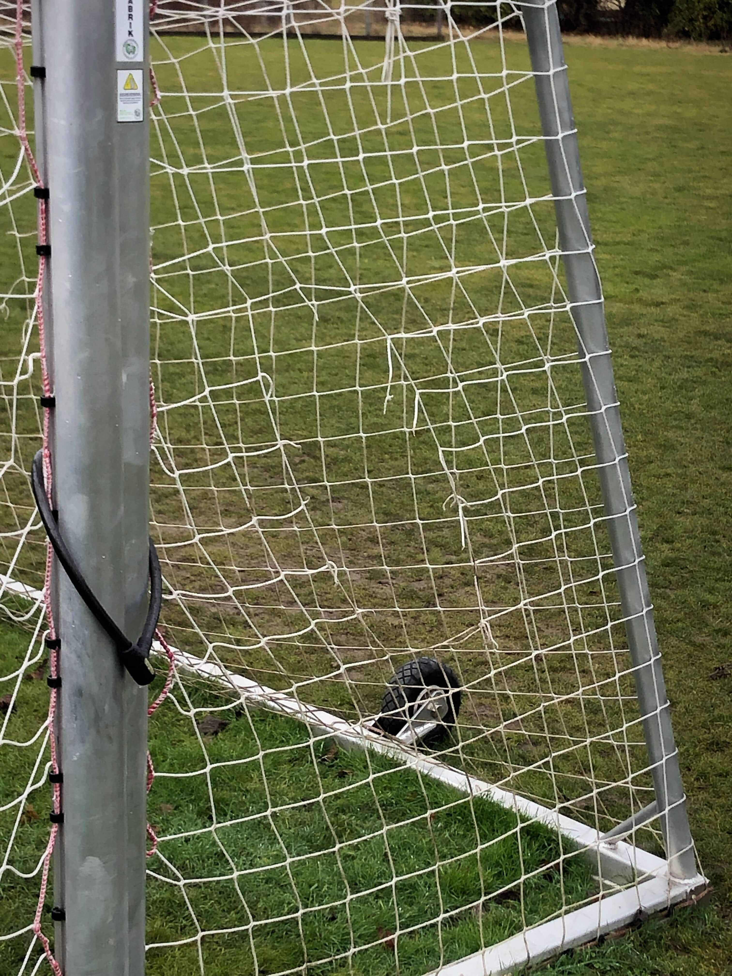 Ein Fußballtor mit einem beschädigten Netz auf einem grünen Rasenplatz. Ein Fußball liegt neben dem Tor.
