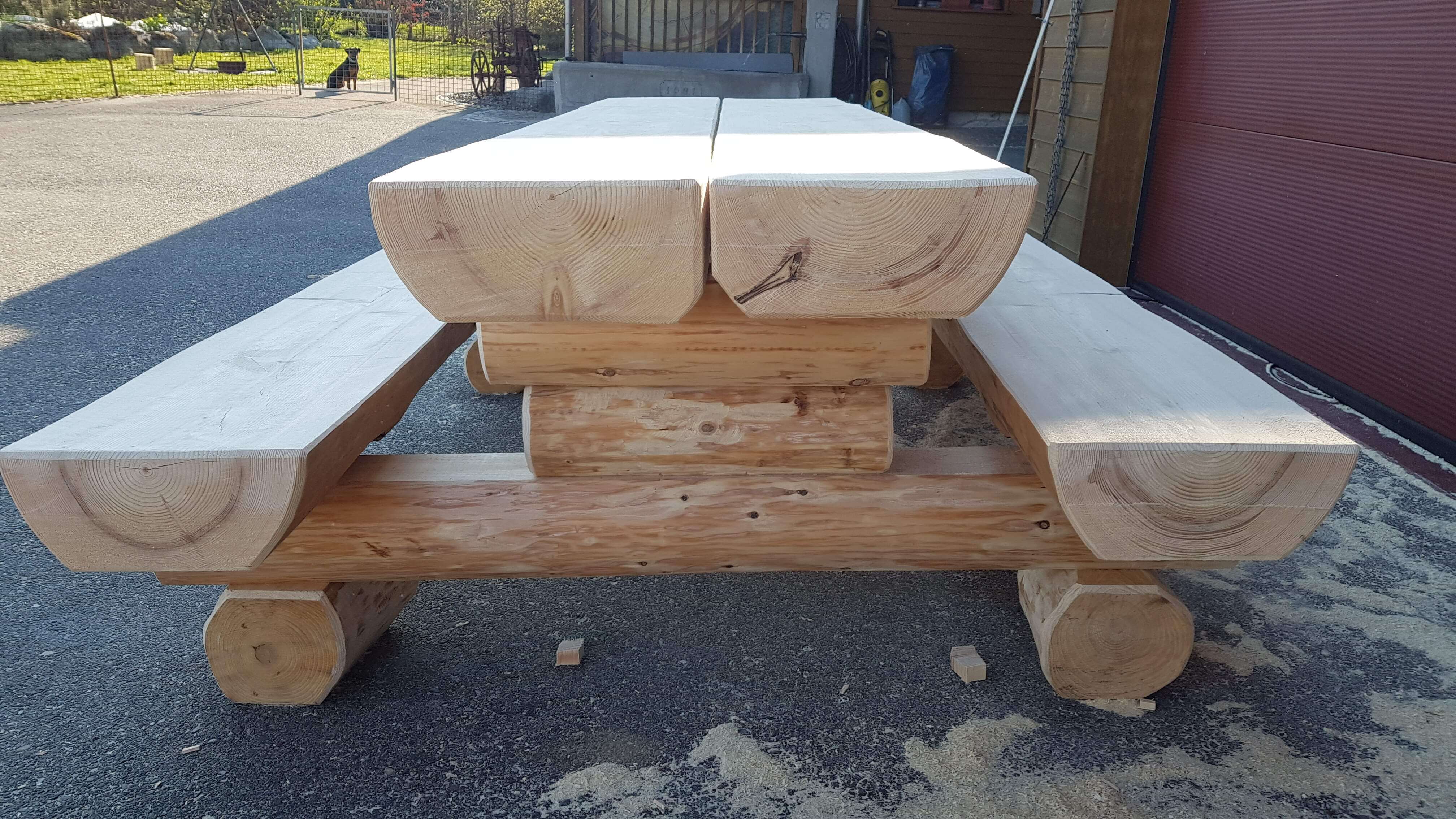 Massiver Holztisch mit integrierten Bänken im Freien aus rohem, hellem Holz.