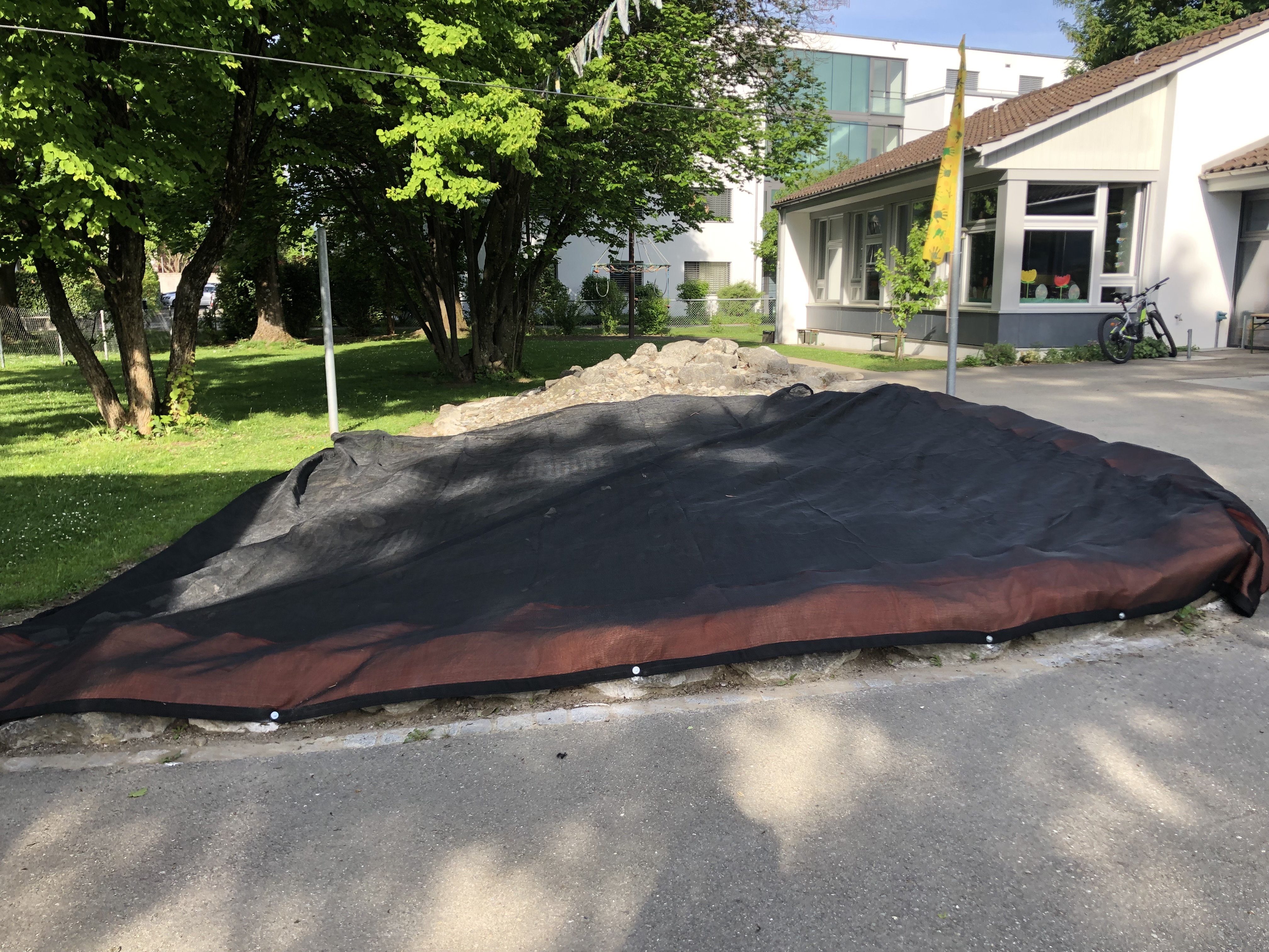 Schwarze Abdeckung über einem Steinhaufen, neben einem Gebäude im Freien