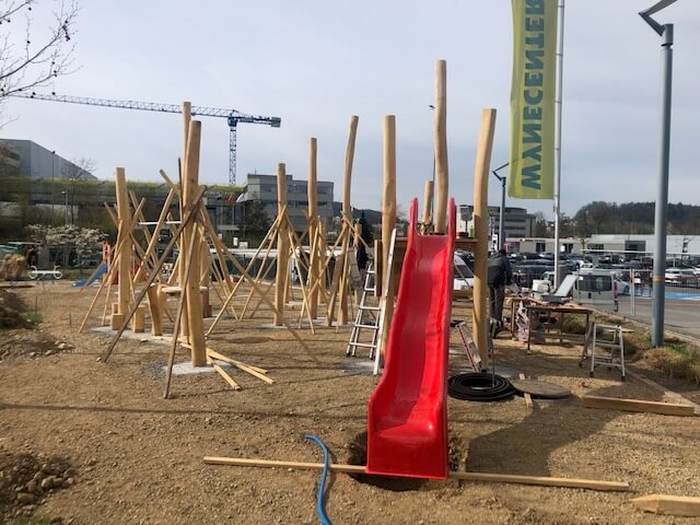 Un chantier de construction d'une aire de jeux avec un toboggan rouge et des structures en bois.