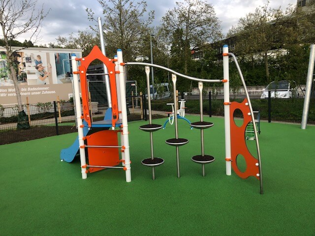 Une aire de jeux moderne avec une structure d'escalade colorée en métal et en plastique, entourée de gazon synthétique vert.