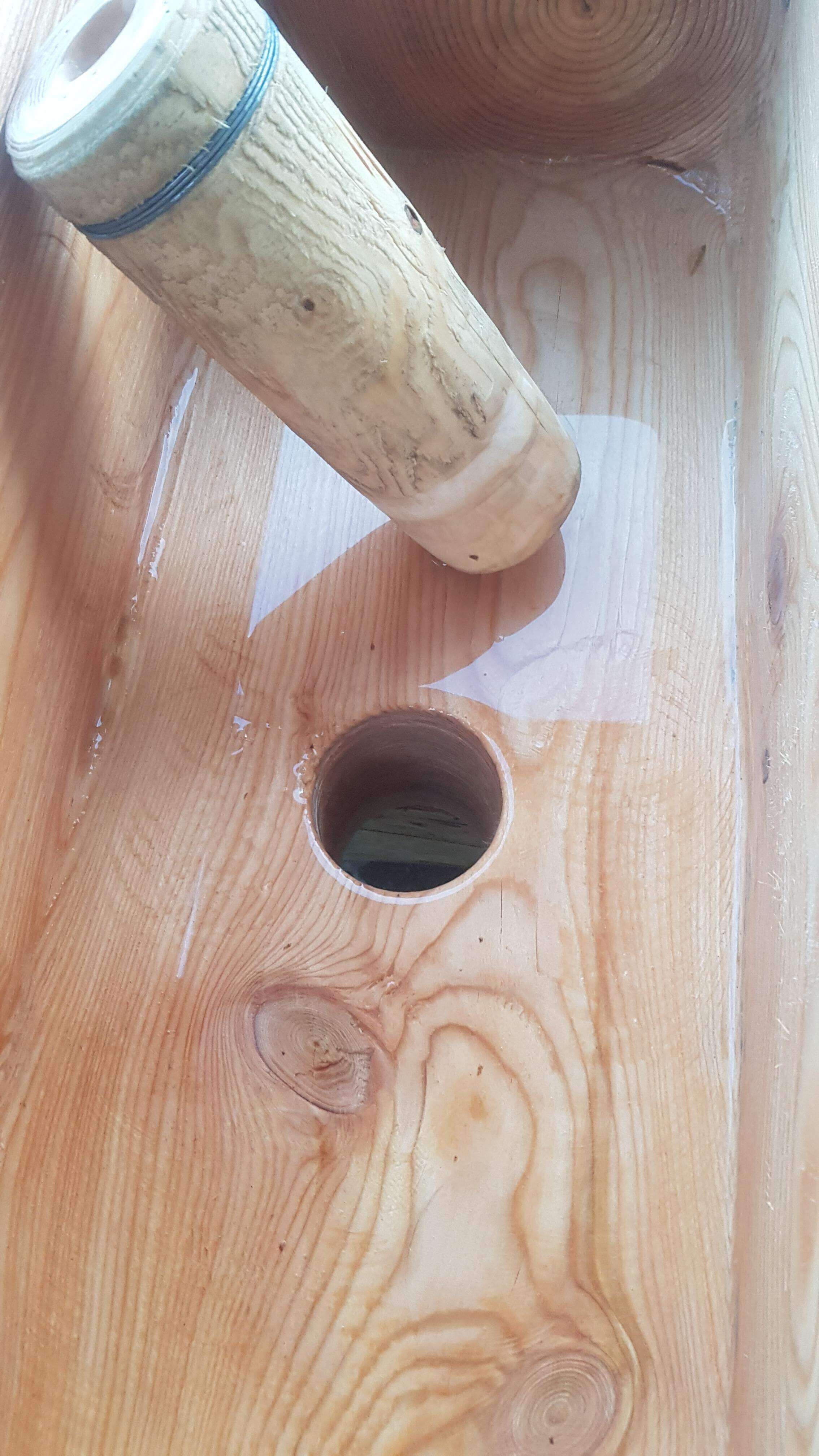 Gros plan sur un lavabo en bois massif avec une ouverture pour l'arrivée d'eau et des veines de bois visibles