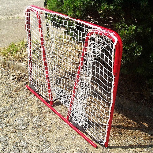 Zwei rote Eishockeytore mit weißen Netzen stehen draußen auf befestigtem Boden neben einem Baum