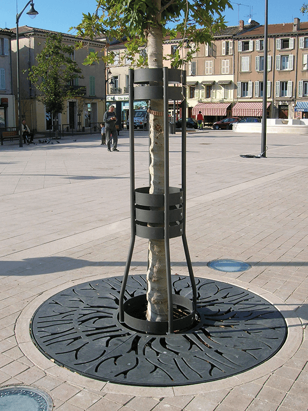 Ein Baum mit einem modernen Metall-Baumschutz auf einem urbanen Platz, umgeben von Pflastersteinen.