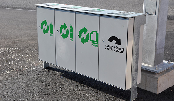 Recyclingstation mit getrennten Behältern für Aluminium, PET, Papier und andere Abfälle auf einem Asphaltuntergrund.