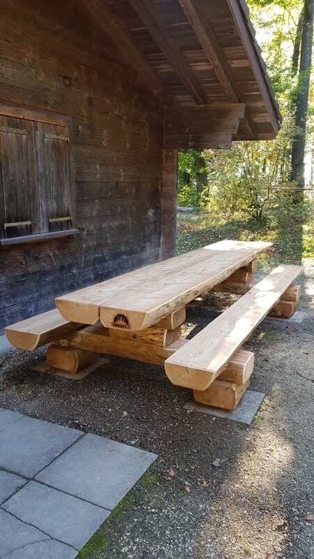 Massiver Holztisch mit Sitzbänken im Freien vor einer Holzhütte