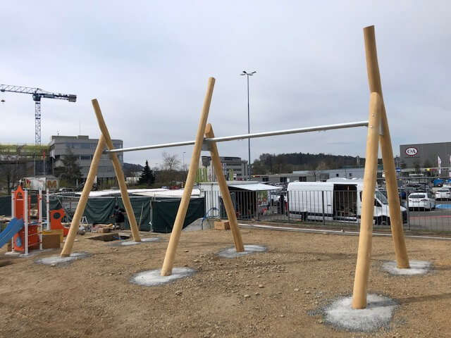 Structure d'aire de jeux en bois inachevée avec poutres inclinées, prise sur un chantier devant une zone industrielle