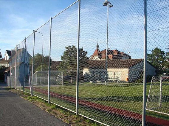 Drahtzaun um einen grünen Sportplatz vor einem alten Gebäude unter blauem Himmel