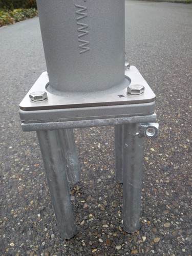 Nahaufnahme einer Metallsäule mit Schrauben und Halterungen auf einer asphaltierten Fläche