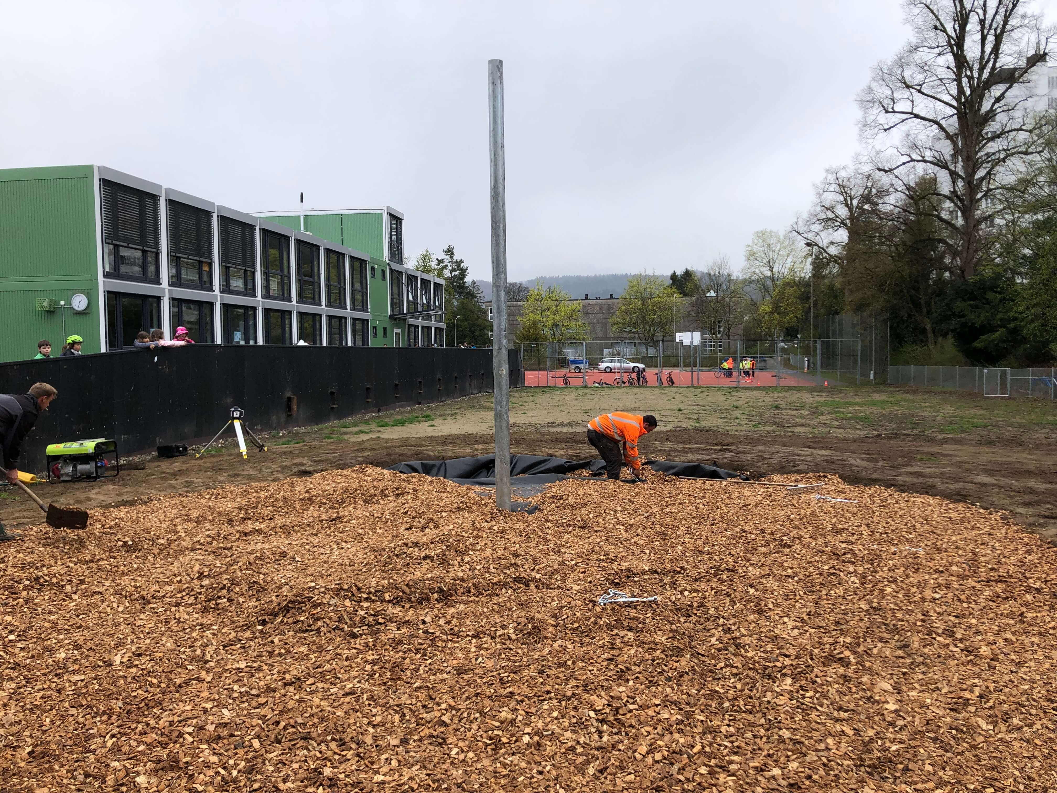 Un chantier de copeaux de bois et deux ouvriers devant un bâtiment à la façade verte