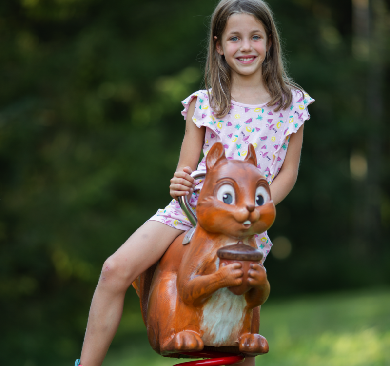 Lächelndes Mädchen auf einer Eichhörnchen-Wippe in einem grünen Park