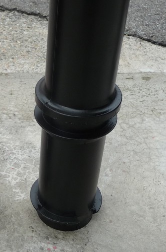 Ein schwarzer Metallpoller steht auf einer Betonoberfläche, möglicherweise zur Verkehrsleitung oder als Sicherheitsvorrichtung.