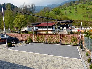 Un parking récemment aménagé avec des pavés gris, entouré d'un paysage verdoyant et d'un bâtiment en arrière-plan.