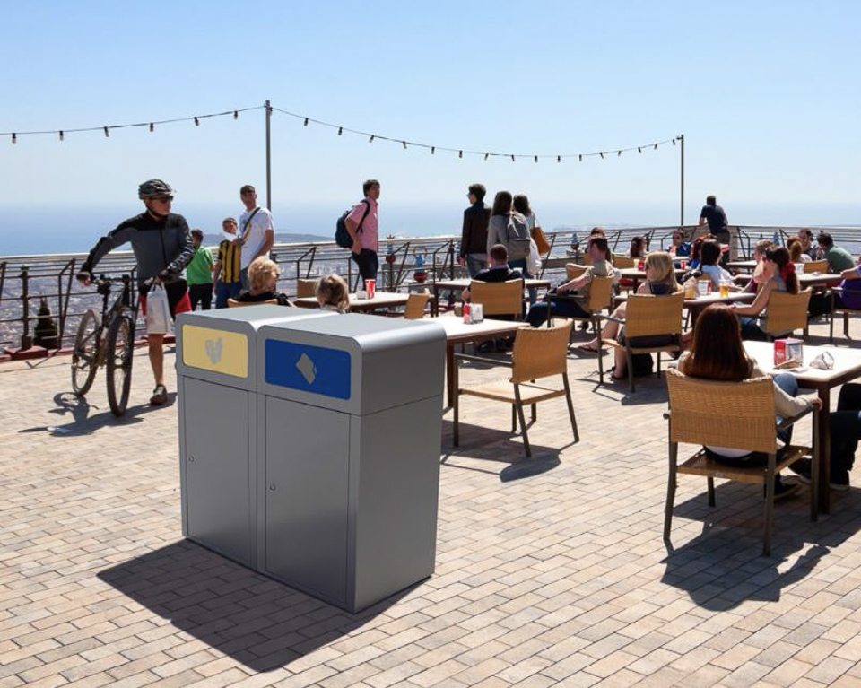 Personnes sur une terrasse ensoleillée d'un café avec des poubelles originales et vue sur la mer
