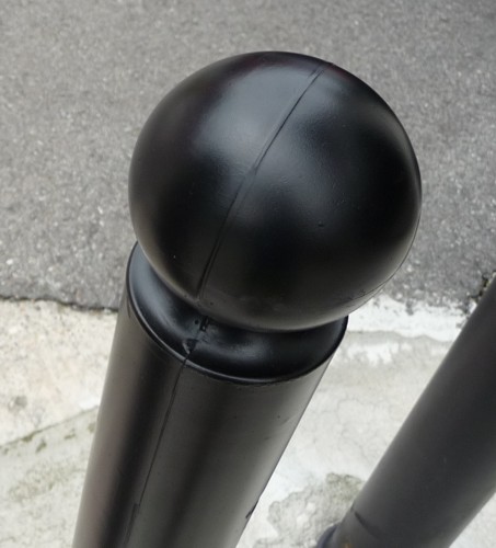 Schwarzer Metallpoller mit kugelförmigem Kopf auf einem Gehweg