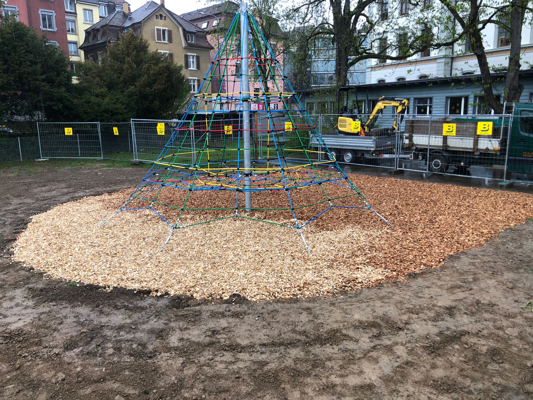 Kletterpyramide mit buntem Kletternetz und Holzmulch auf Spielplatz in städtischer Umgebung