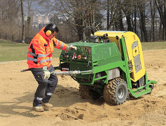 Un homme en vêtements de signalisation travaille avec une machine de construction verte sur une surface sablonneuse en plein air