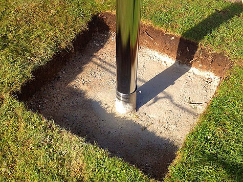 Un poteau en acier inoxydable solidement ancré dans une fondation carrée en béton dans le gazon