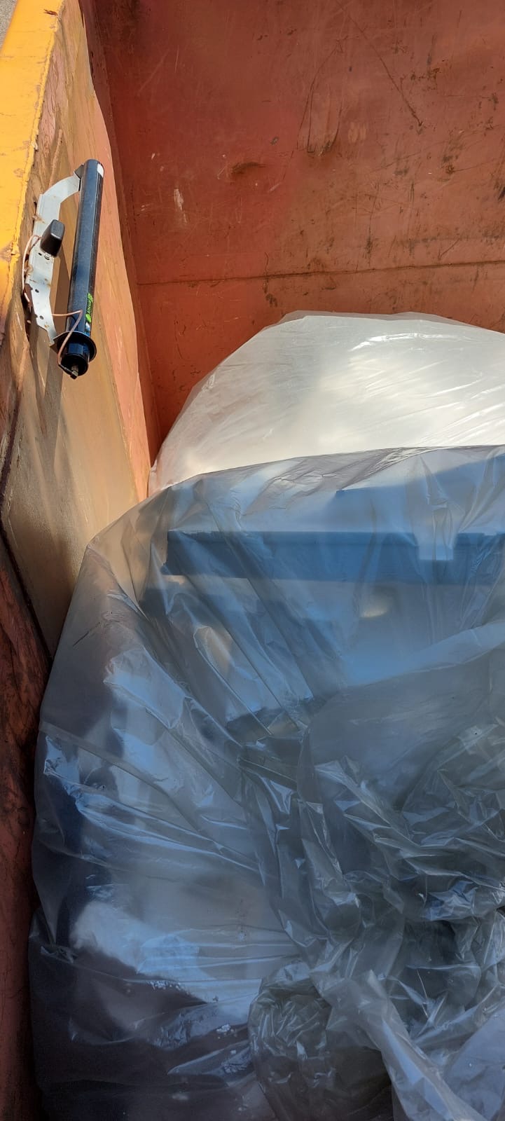 Eine große weiße Plastiktüte liegt in einem rostigen Container aus Metall.