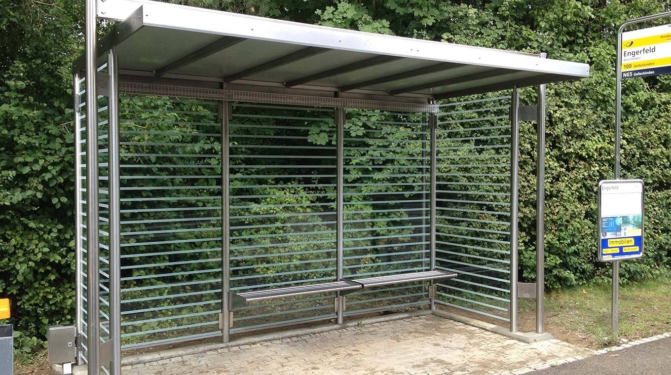 Arrêt de bus avec parois en verre, banc en métal et toit dans un environnement vert
