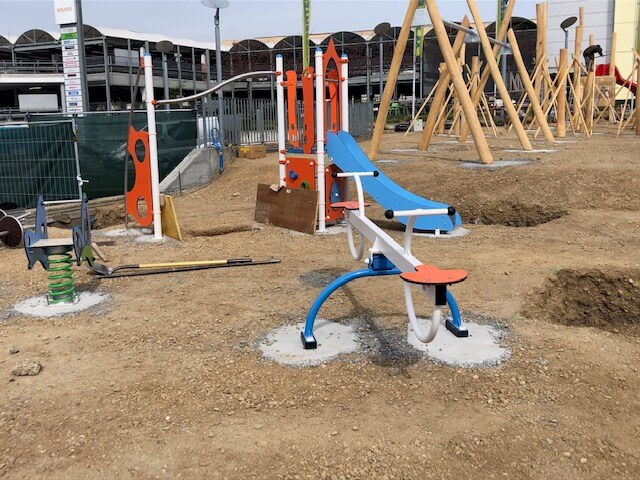 Une aire de jeux inachevée avec une bascule et un toboggan colorés, entourée de matériaux de construction.