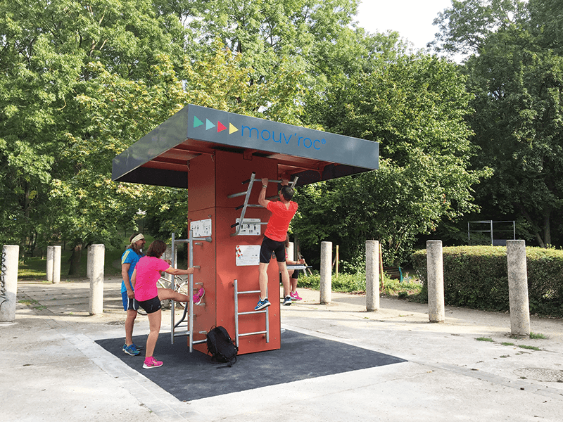 Gruppe von Menschen nutzt eine Outdoor-Fitnessstation im Freien, um verschiedene Übungen zu machen, umgeben von grünen Bäumen.