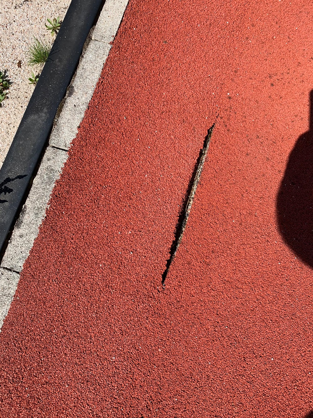 Une fissure dans une piste de course rouge près d'un bord de pavé.