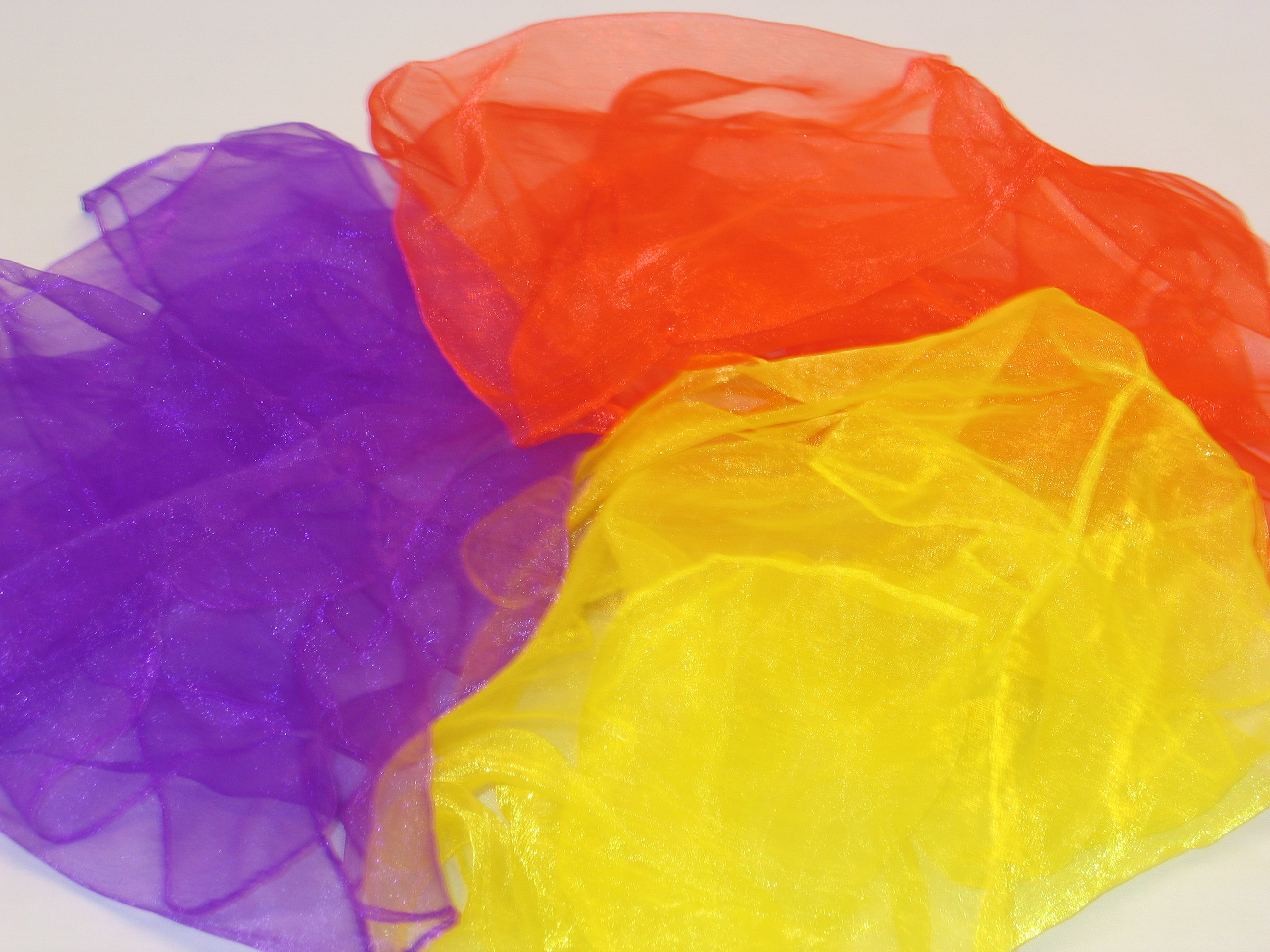 Drei transparente Chiffontücher in den Farben Violett, Rot und Gelb übereinandergelegt