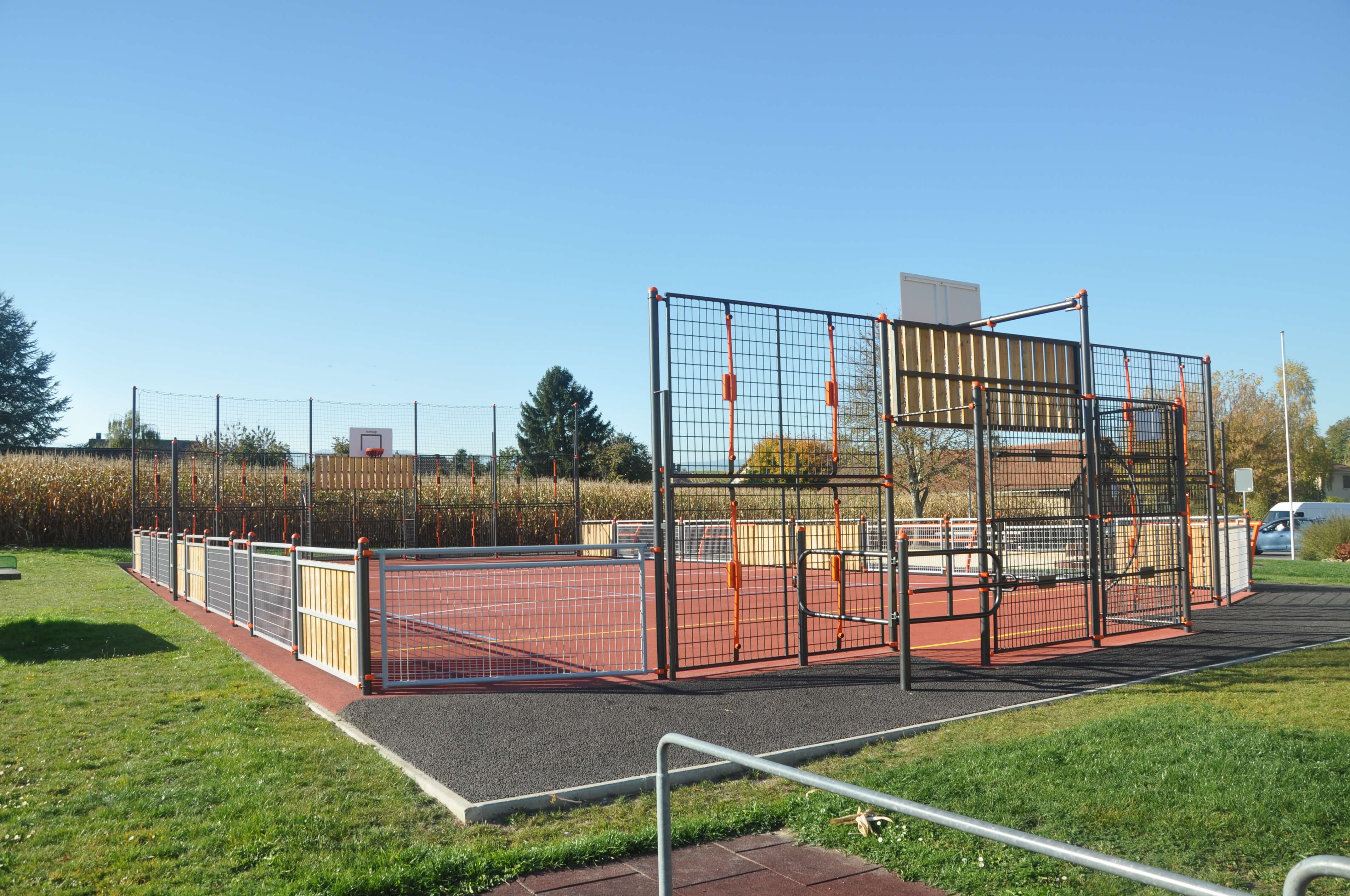 Un terrain de basket moderne avec une clôture de protection, entouré de pelouse verte et d'arbres, par une journée ensoleillée