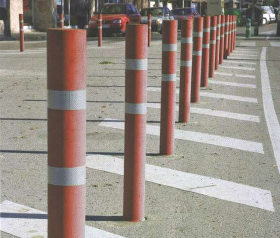 Mehrere rot-weiße Absperrpoller, die auf einer Straße in einer geraden Linie angeordnet sind, mit Autos im Hintergrund.
