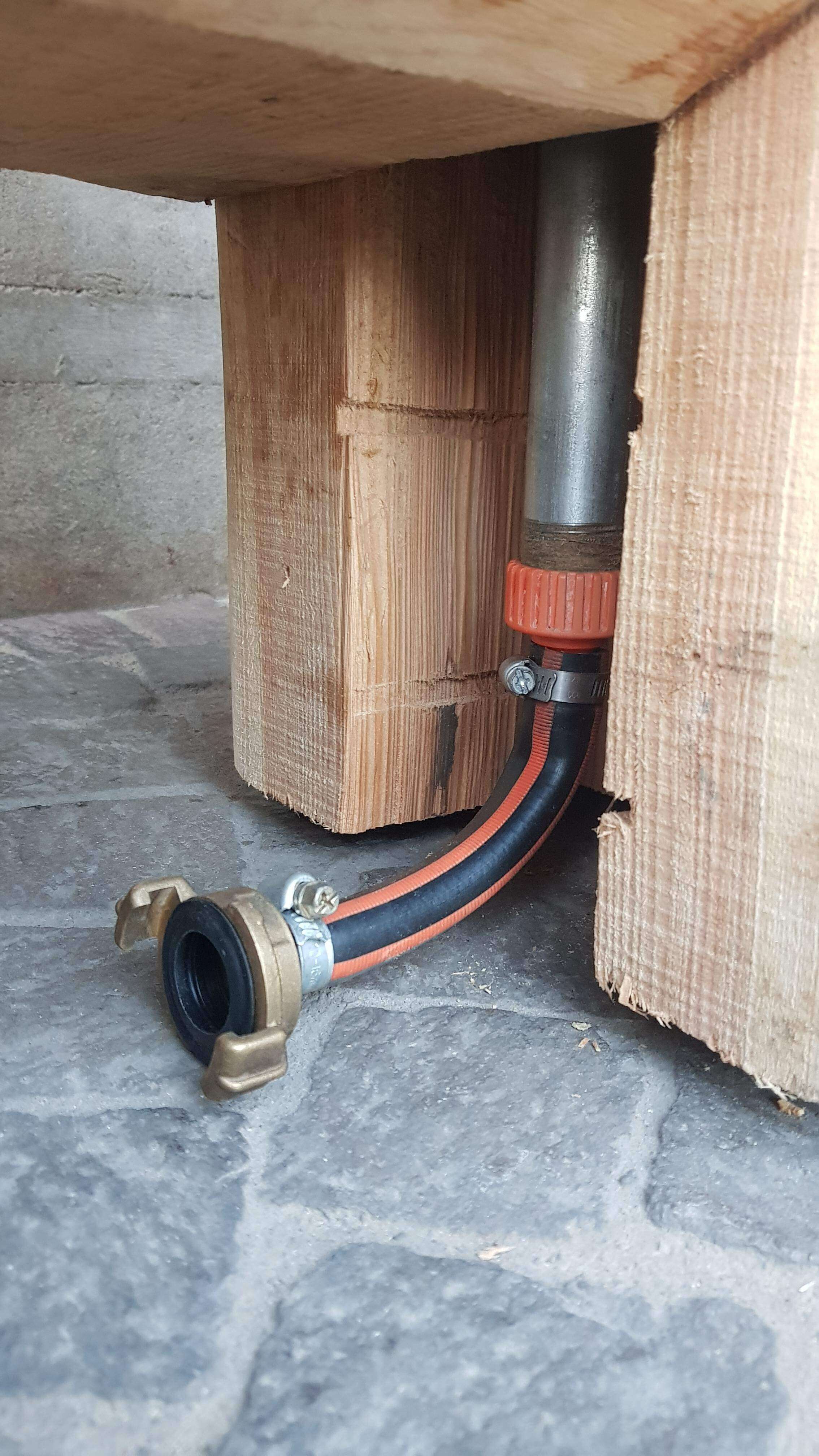 Une prise d'eau avec un tuyau orange et un raccord métallique sous une structure en bois.