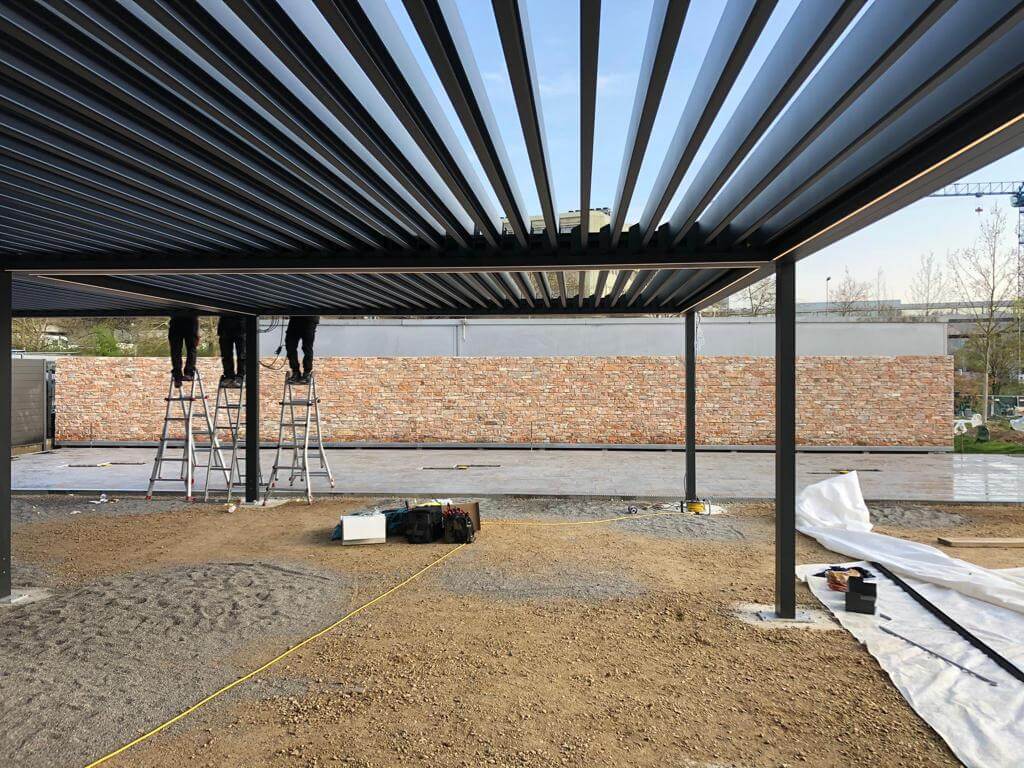 Des ouvriers installent une toiture métallique sur une terrasse, avec un mur de briques en arrière-plan