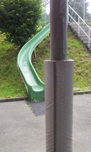 Spielplatz mit grüner Rutsche und gepolstertem Pfosten vor einer Treppe