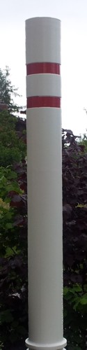 Ein weißer Poller mit zwei roten Streifen, aufgestellt im Grünen eines Gartens.