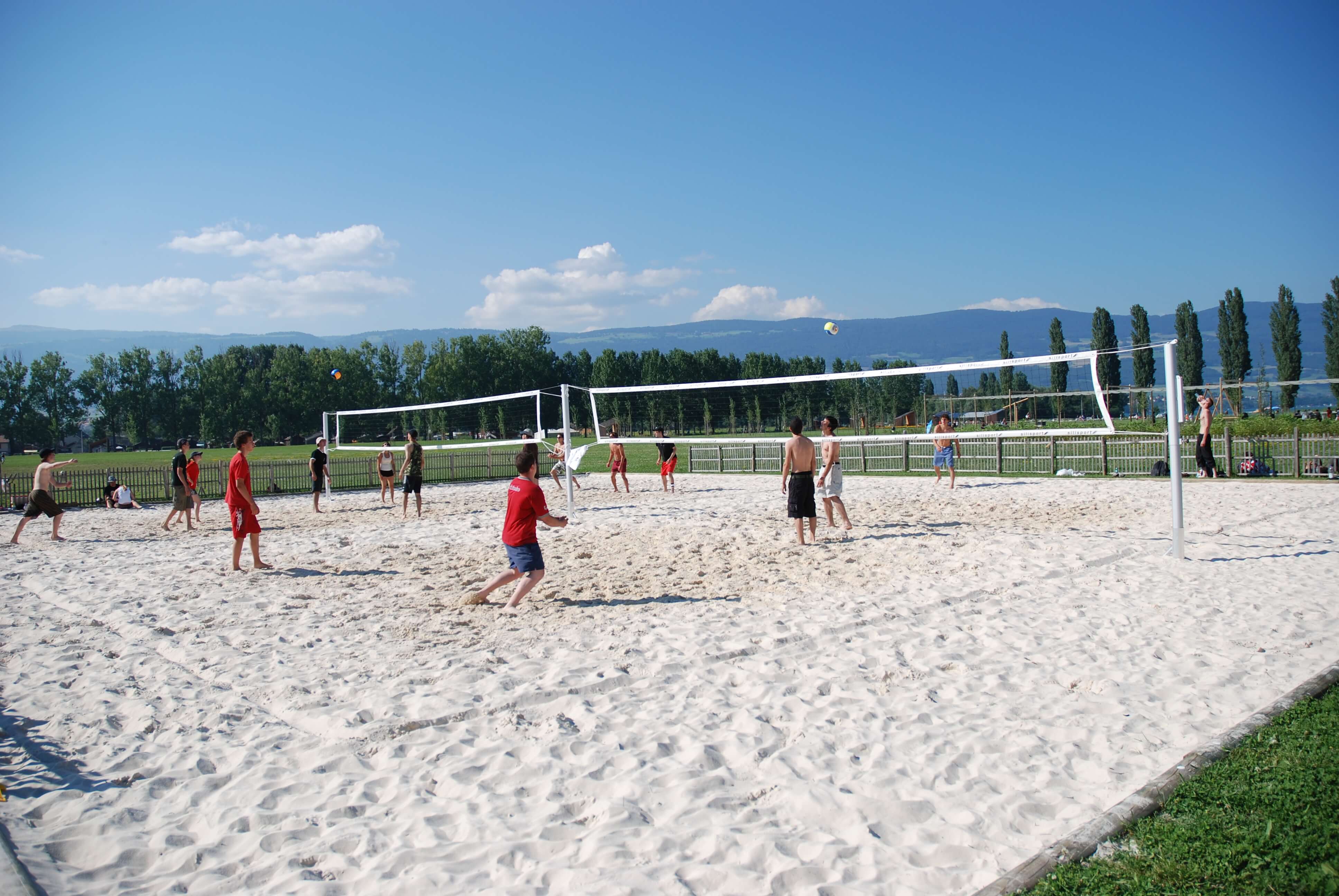 Un groupe d'adolescents joue au beach-volley sur un terrain de sable sous un ciel bleu