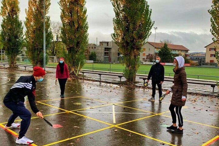 Menschen spielen Tischtennis auf einem nassen Sportplatz mit Bäumen im Hintergrund