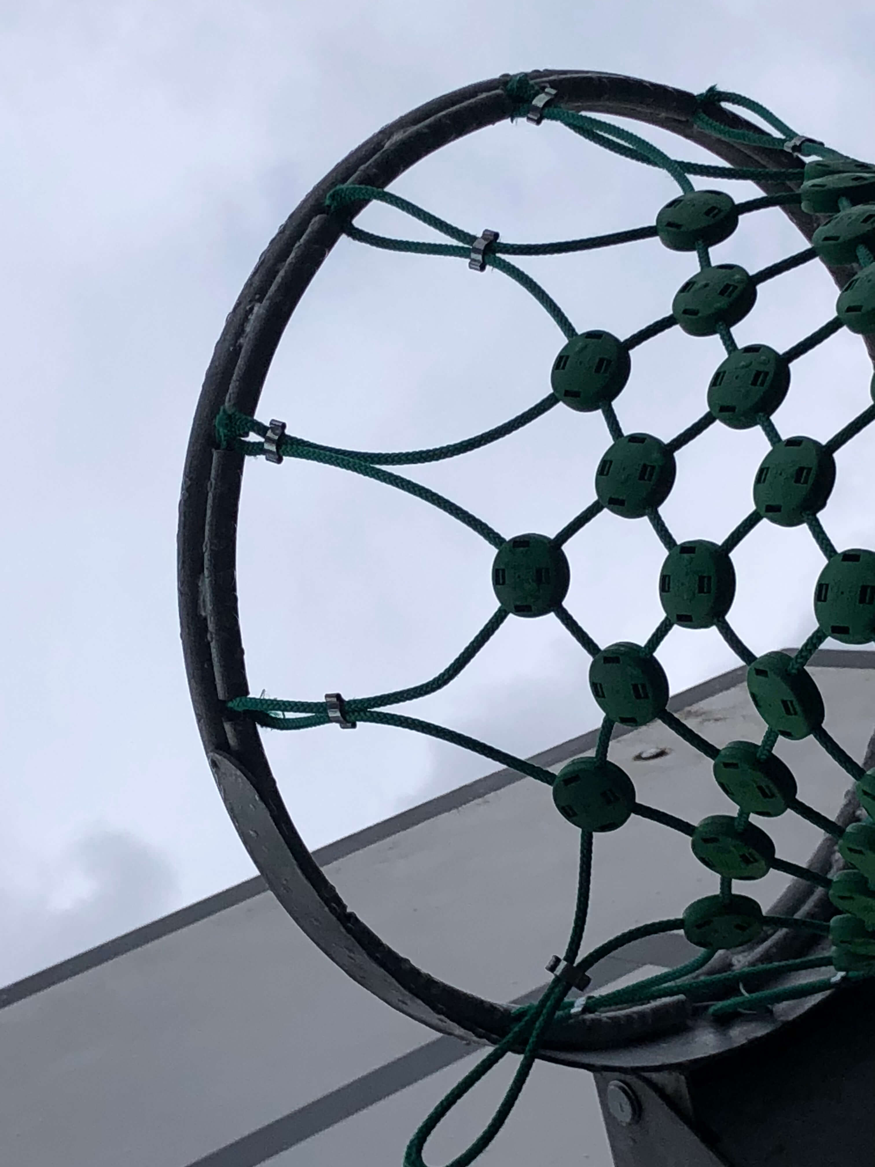 Nahaufnahme eines Basketballkorbs mit einem grünen Netz, der gegen einen bewölkten Himmel gerichtet ist