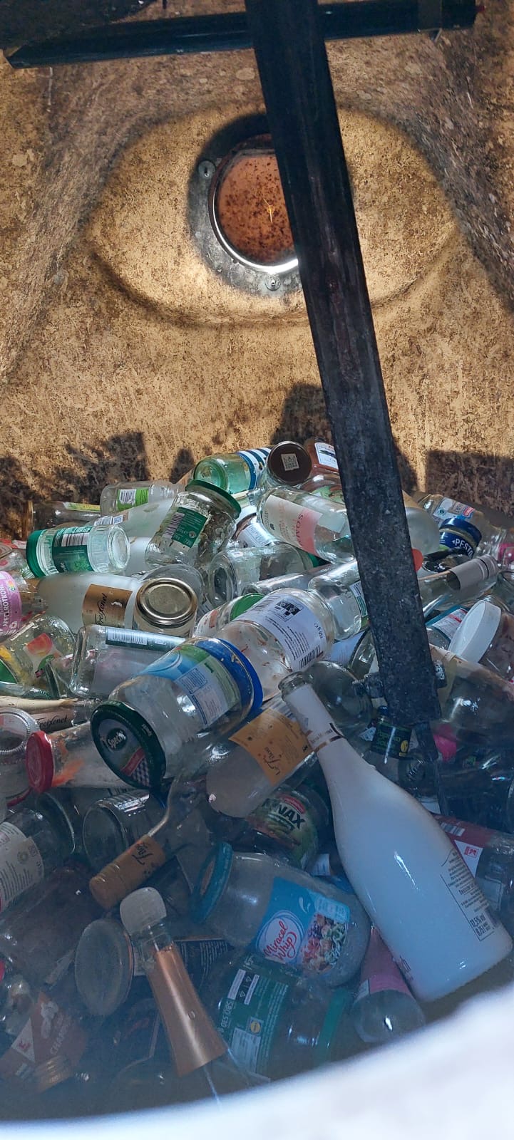 Ein Blick in einen Container mit zahlreichen leeren Glasflaschen und Gläsern, bereit für das Recycling.