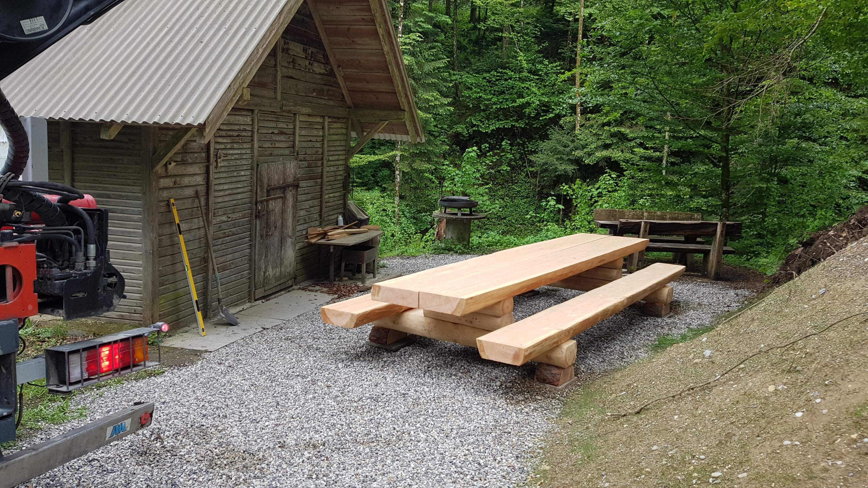 Rustikaler Holztisch mit Bänken neben einer Holzhütte im Wald, umgeben von Bäumen und Natur