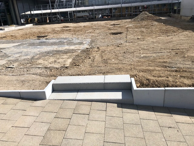 Un chantier avec des dalles de sol nouvellement posées et un petit escalier qui mène à une terre. Des échafaudages sont visibles à l'arrière-plan.